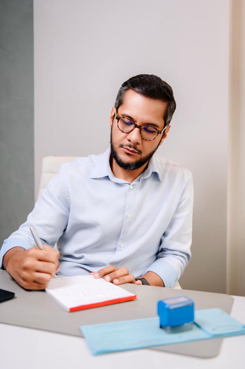 Dr. Rodrigo D'Oliveira escrevendo em seu consultório